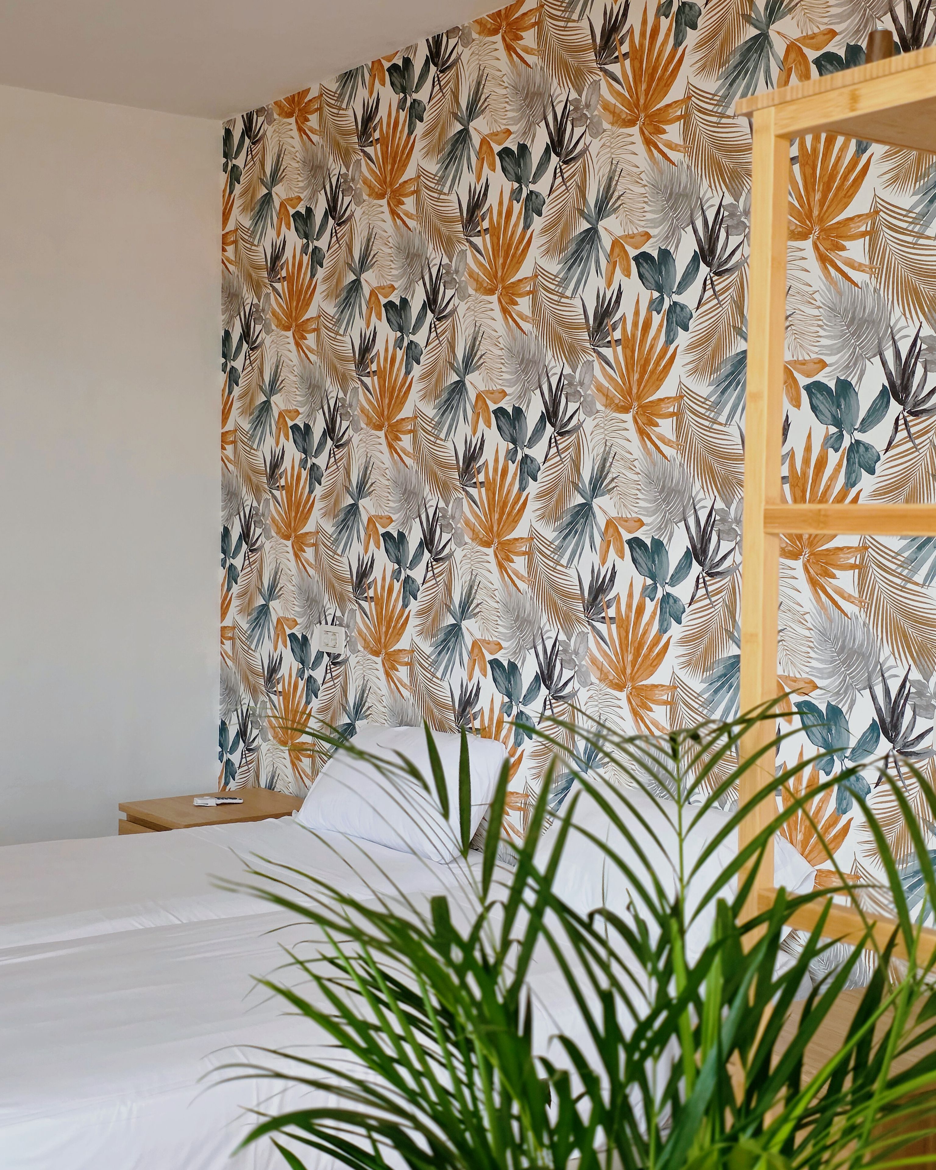 Une chambre avec un lit, une tête de lit en bois et un mur orné d’un motif de feuilles tropicales.