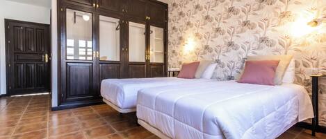 A hotel room with two beds, a wardrobe, and a floral wallpaper.