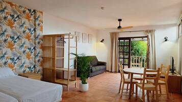 A hotel room with a bed, a seating area with a table and chairs, a potted plant, and a balcony with a view.