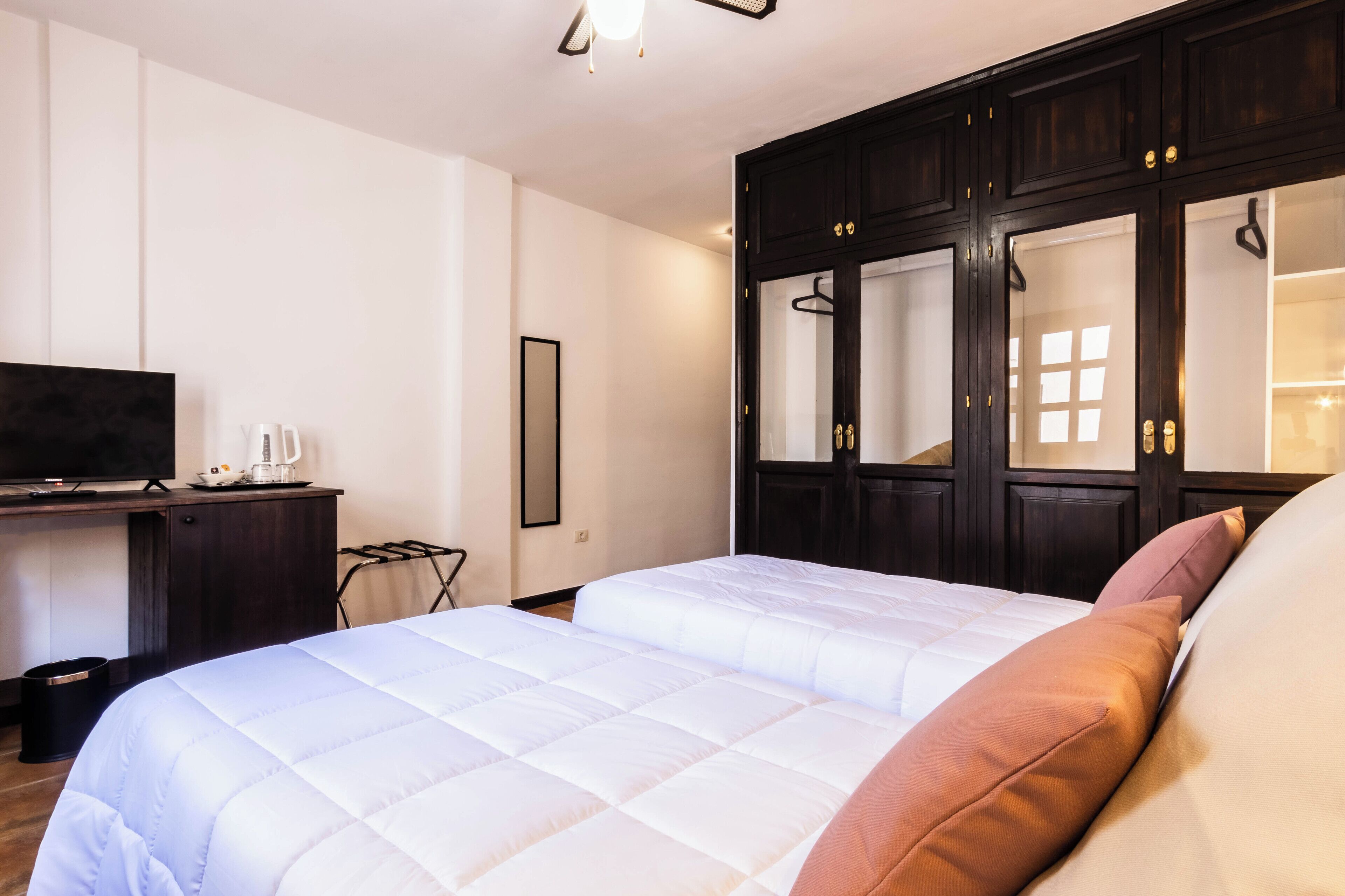 A bedroom with a large bed, a TV, a wardrobe, and a desk.