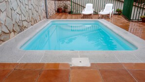 A rectangular swimming pool with a stone wall on one side and a tiled patio area with two white lounge chairs and potted plants. - Holiday Home 'Batalla Navas de Tolosa' with Mountain View, Pool & Wi-Fi (Santa Elena)