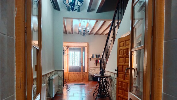 A hallway with a wooden door, a radiator, a sewing machine, and a staircase with a wrought iron railing. - Holiday Home 'Batalla Navas de Tolosa' with Mountain View, Pool & Wi-Fi (Santa Elena)