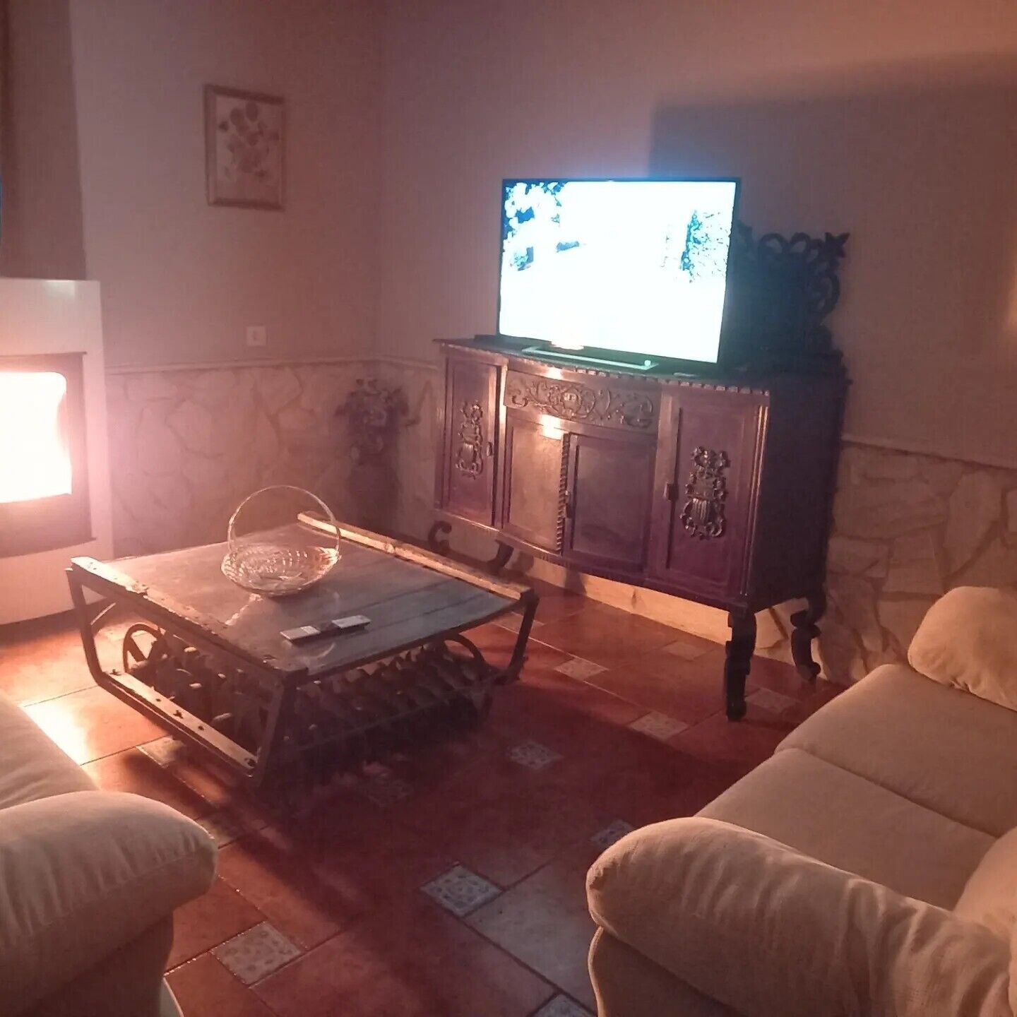 Una sala de estar con un televisor sobre un mueble de madera, una mesa de centro de vidrio y dos sofás.