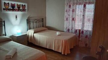 Un dormitori amb dos llits, una tauleta de nit, aire condicionat fixat a la paret i una finestra amb cortines florals.