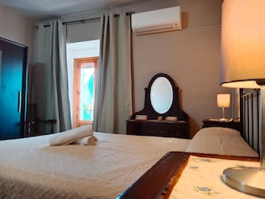 A hotel room with a bed, a dresser, a mirror, a lamp, and an air conditioning unit.