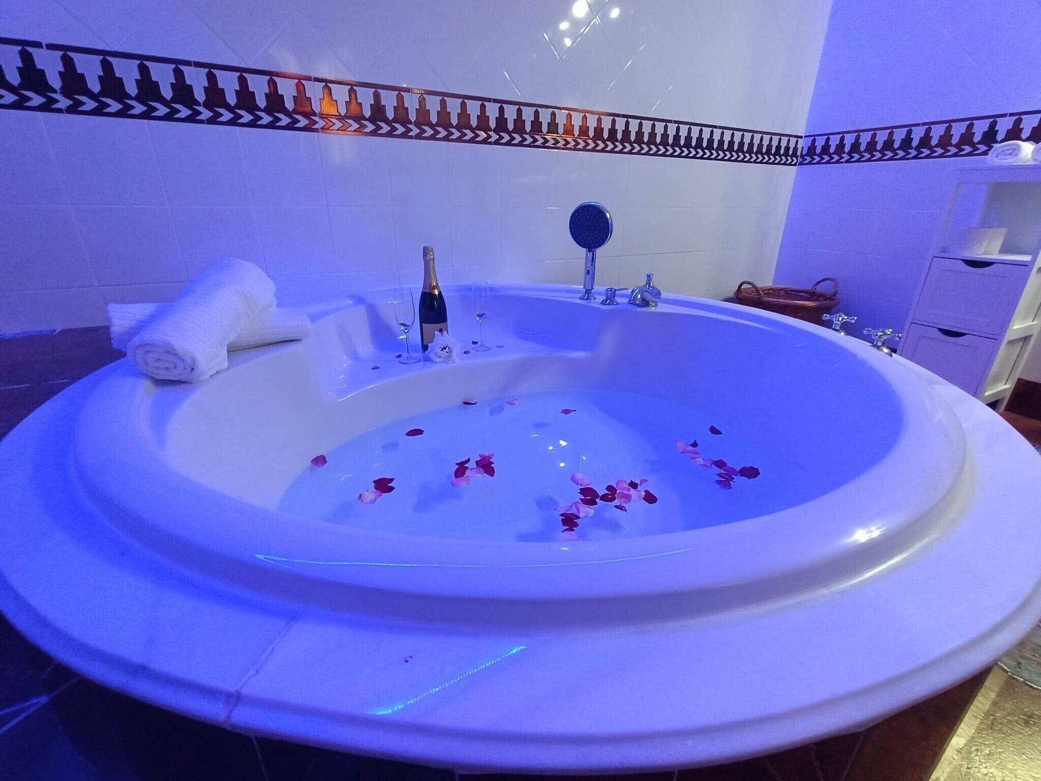 Una vasca da bagno ampia con petali di rosa, una bottiglia e dei bicchieri, che suggeriscono un'atmosfera romantica.