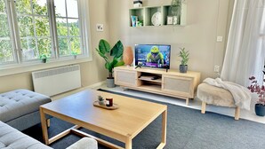En moderne stue med en sofa, et sofabord, et fjernsyn på et træstel og et vindue med persienner.