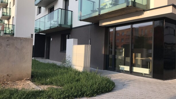 A modern building with glass balconies, a paved walkway, and a small garden area.