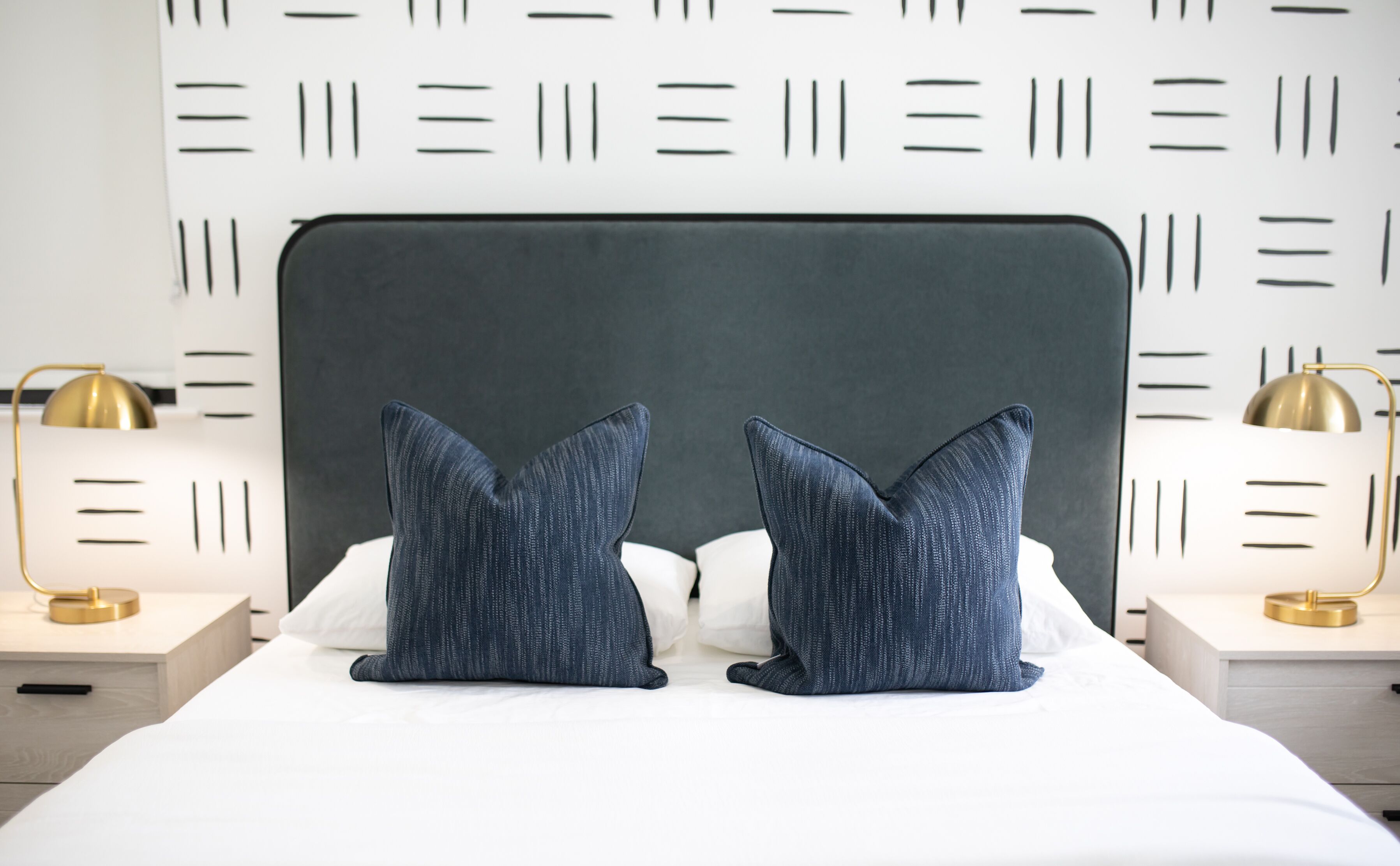 A bed with a dark headboard, two matching pillows, and two bedside lamps with gold bases.