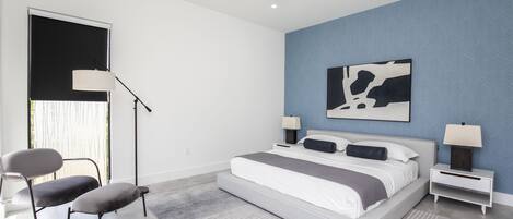 Un dormitorio moderno con una cama grande, dos mesitas de noche, un ventilador de techo y un amplio ventanal con persianas.