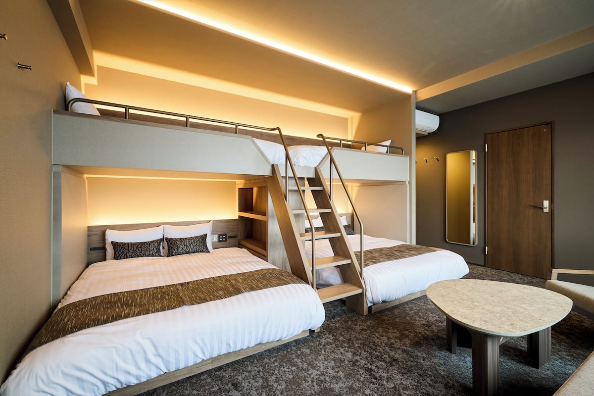 A hotel room with two beds, a small table, and a staircase connecting the beds.
