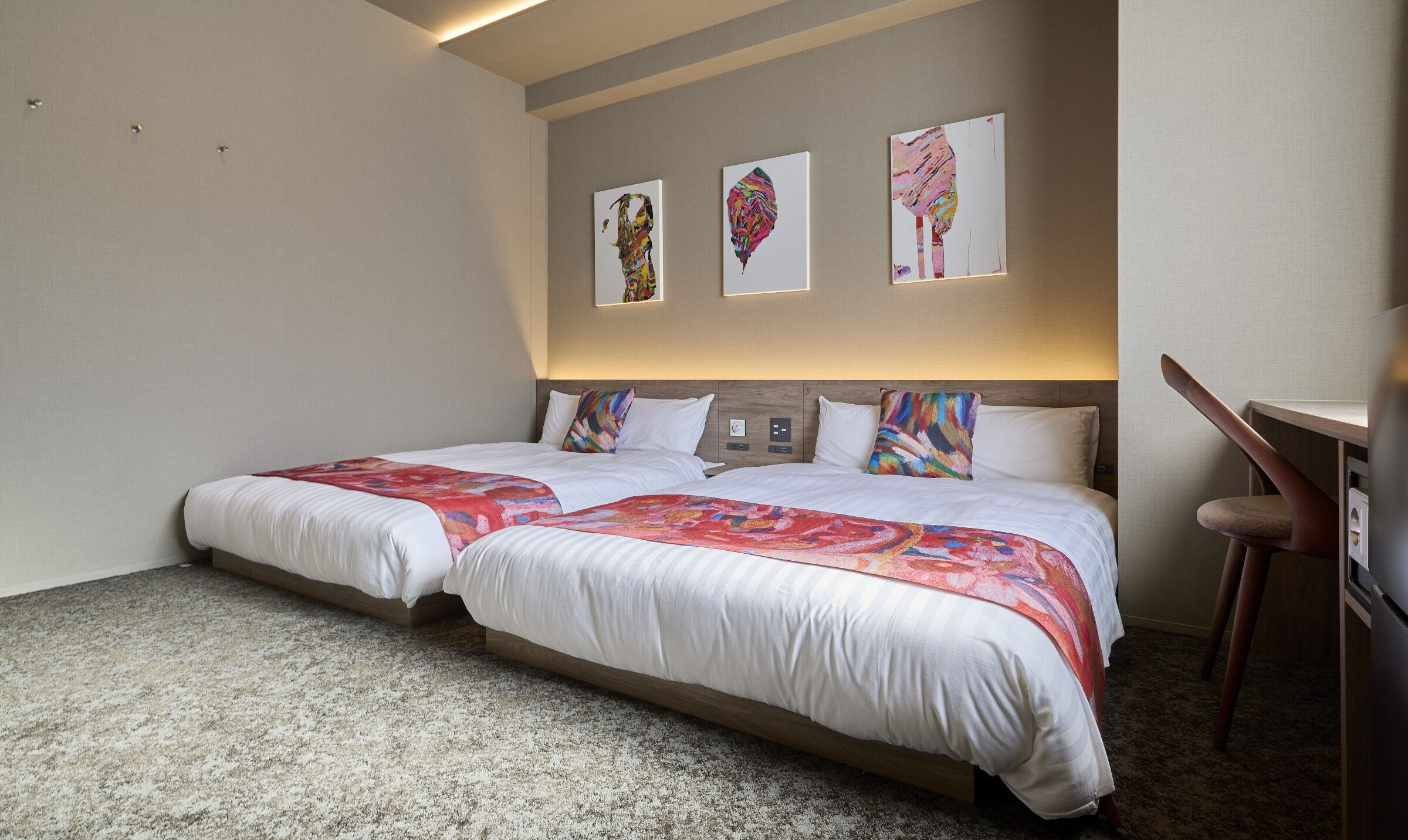 Une chambre d’hôtel avec deux lits, un bureau et trois tableaux abstraits accrochés au mur.