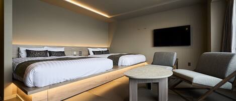 Una habitación de hotel moderna con una cama grande, un televisor montado en la pared y una zona de estar con una mesa y sillas.