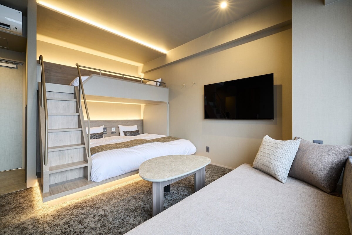 A modern hotel room with a bunk bed, a small table, and a flat-screen TV mounted on the wall.