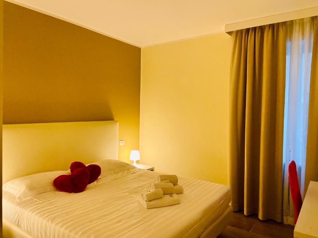 A hotel room with a bed, a nightstand, a lamp, and a window with curtains.