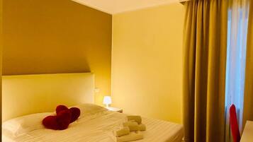 A hotel room with a bed, a nightstand, a lamp, and a window with curtains.
