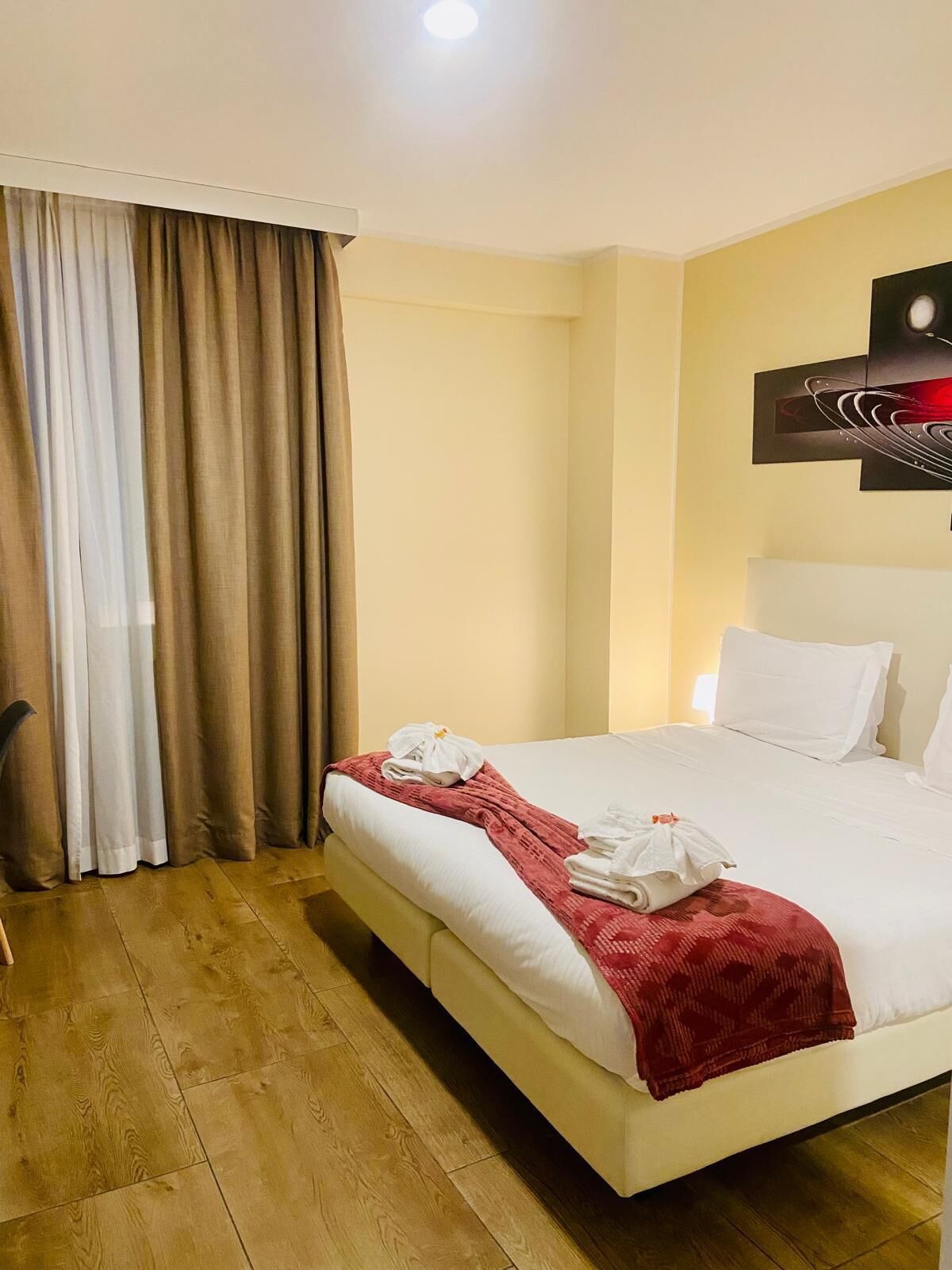 Quarto de hotel com uma cama grande, um cobertor vermelho, almofadas brancas e uma pintura na parede.