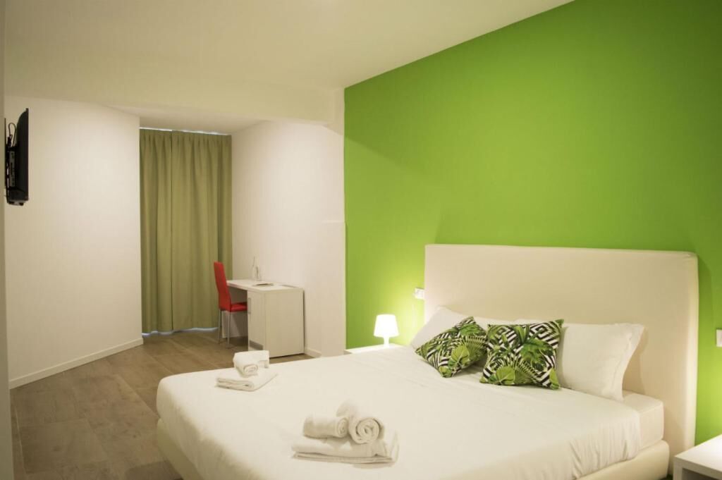 A hotel room with a bed, a desk, a chair, and a green accent wall.