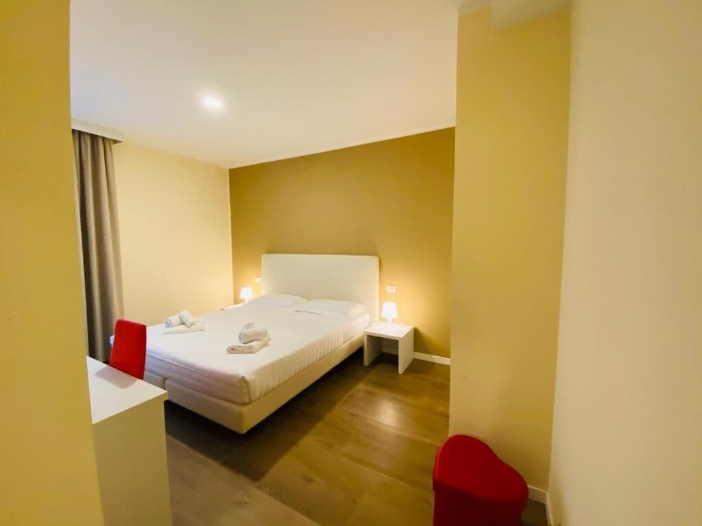 A hotel room with a bed, a nightstand, a red chair, and a desk.