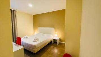 A hotel room with a bed, a nightstand, a red chair, and a desk.