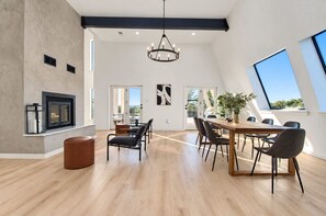 A spacious living area with a dining table, chairs, a fireplace, and large windows. - Modern Home - 1 Acre Lot w/ Pool, Patios, Jacuzzi (Denton)