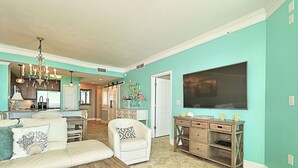 A spacious living room with a large flat-screen TV, a white sofa, and a wooden coffee table. - Amazing 3 Bedroom 3 bath overlooking the breathtaking emerald coast water. (Panama City Beach)