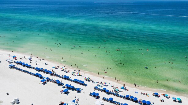 A beach with rows of blue umbrellas and sun loungers, clear turquoise water, and a sandy shore. - Amazing 3 Bedroom 3 bath overlooking the breathtaking emerald coast water. (Panama City Beach)