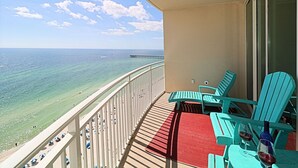 A balcony with turquoise chairs, a red mat, and two glasses of red wine. - Amazing 3 Bedroom 3 bath overlooking the breathtaking emerald coast water. (Panama City Beach)
