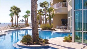 A swimming pool with palm trees, a sun terrace, and a building with a balcony. - Amazing 3 Bedroom 3 bath overlooking the breathtaking emerald coast water. (Panama City Beach)
