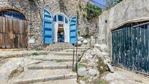 A stone building with a staircase leading to a door with blue shutters, a wooden door, and a metal gate.