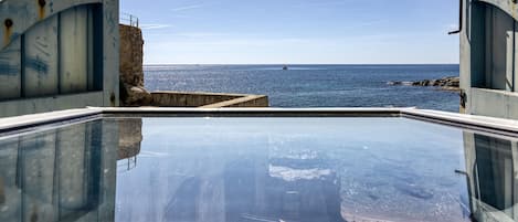 A pool with a clear view of the sea and a rocky coastline.