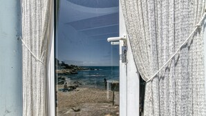 A window with a view of a beach, a rocky shoreline, and a clear sky.