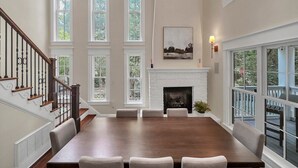 A spacious dining room with a large wooden table and six chairs, a fireplace, and a staircase with wooden railings. - Private Pool,LSV/Golf Cart, & 6 Bikes! Steps to Seaside in the Heart of Old Seagrove! (Santa Rosa Beach)