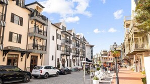 A street with multi-story buildings, parked cars, and outdoor seating areas. - Private Pool,LSV/Golf Cart, & 6 Bikes! Steps to Seaside in the Heart of Old Seagrove! (Santa Rosa Beach)