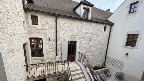 A stone building with a staircase leading to a balcony with outdoor seating. - La Bastide De Chassagne-montrachet (Chassagne-Montrachet)
