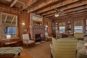 A cozy cabin interior with a brick fireplace, wicker furniture, and wooden beams.