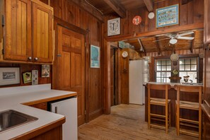 A wooden interior with a kitchen area, wooden cabinets, a refrigerator, and a dining area with two chairs.
