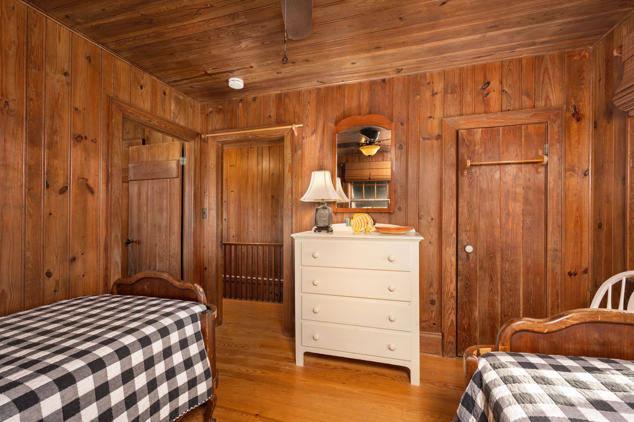 A wooden-paneled room with two beds, a dresser, and a ceiling fan.