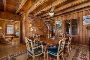 A wooden interior with a dining table, chairs, a staircase, and a ceiling fan.