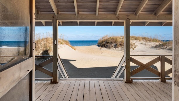 A wooden deck leading to a beach with a clear view of the ocean. - Fred Wood Cottage:Oceanfront, historic, Old Nags Head Style cottage, wide decks! (Nags Head)
