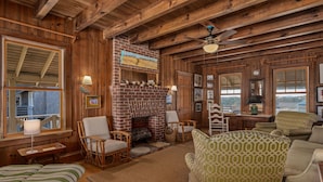 A cozy cabin interior with a brick fireplace, wicker furniture, and wooden beams. - Fred Wood Cottage:Oceanfront, historic, Old Nags Head Style cottage, wide decks! (Nags Head)