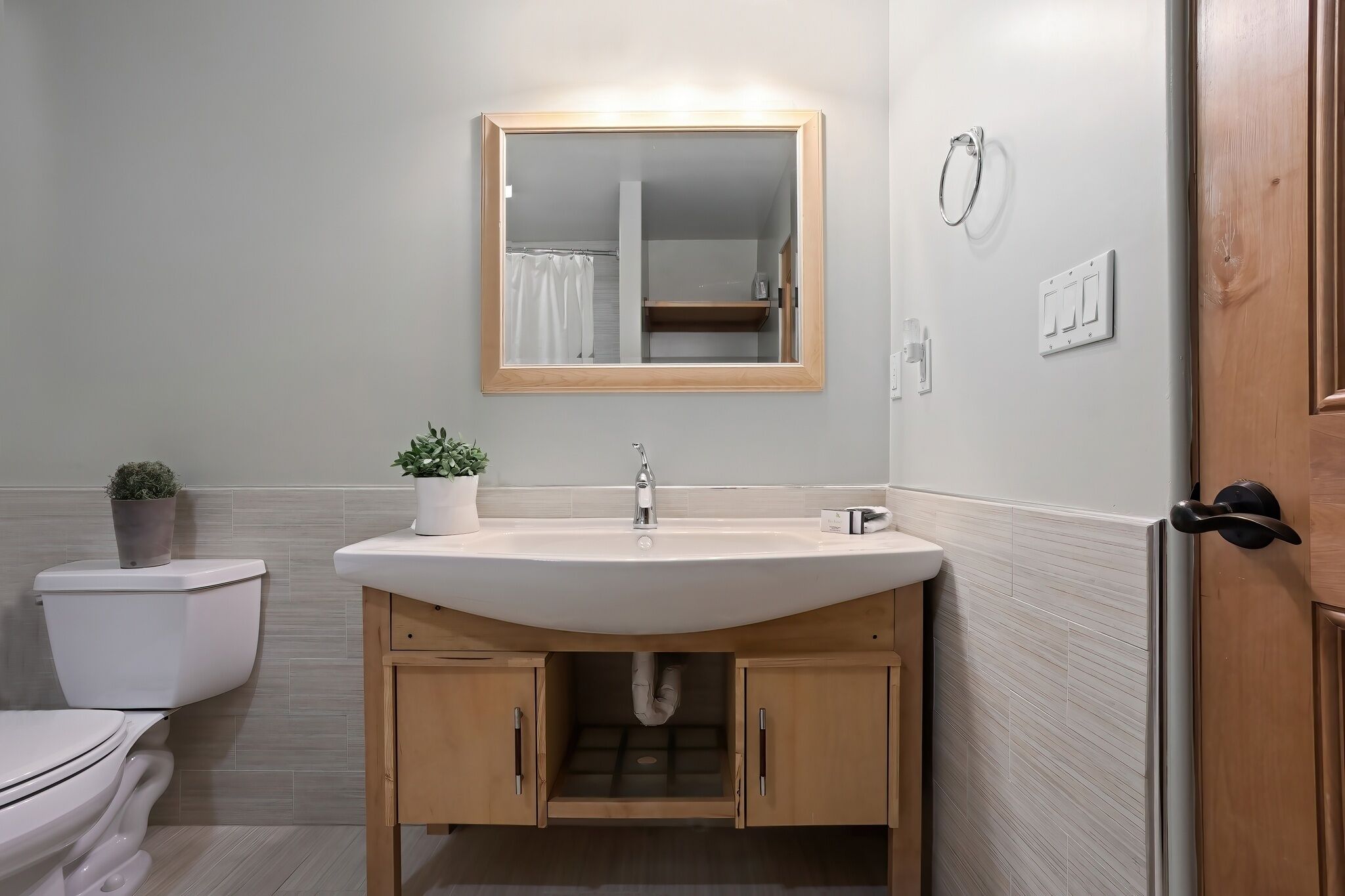 Ein Badezimmer mit Waschbecken, Holzschränken, einem Spiegel und einer Toilette.
