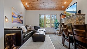 A modern living room with a black leather sofa, a wooden coffee table, and a stone fireplace. - Modern Condo - EV Charger - SM 301 by Bear Valley Vacation Rentals (Arnold)
