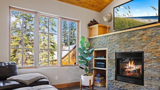 A cozy living room with a fireplace, large windows, and a potted plant. - Modern Condo - EV Charger - SM 301 by Bear Valley Vacation Rentals (Arnold)