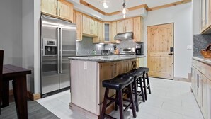 A modern kitchen with wooden cabinets, stainless steel appliances, and a central island with bar stools. - Modern Condo - EV Charger - SM 301 by Bear Valley Vacation Rentals (Arnold)