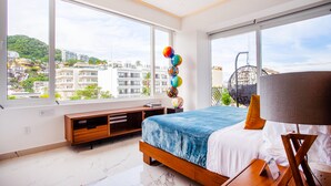 Een moderne hotelkamer met een groot bed, houten meubels en grote ramen met uitzicht op de stad.