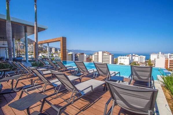 A poolside area with lounge chairs and a view of the ocean and buildings.