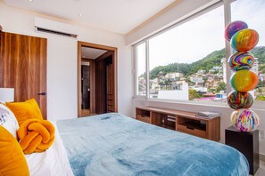 A bedroom with a bed, a window with a view of a cityscape, and a wooden door.