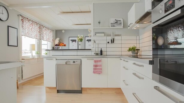 A modern kitchen with white cabinetry, a dishwasher, an oven, and a window with patterned curtains. - RIBO Apartment Arctic - Hostel (Kiruna)