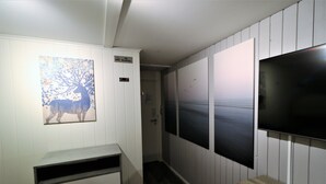 A hallway with a painting of a deer, a TV mounted on the wall, and a bench. - RIBO Apartment Arctic - Hostel (Kiruna)